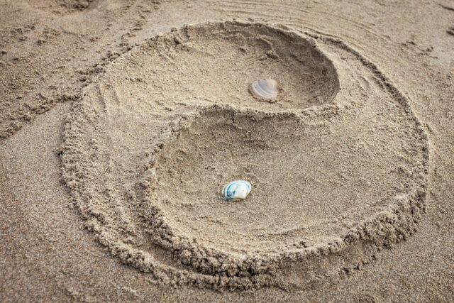 A yin yang design sculpted in sand with seashells at Isla Canela beach, Spain.